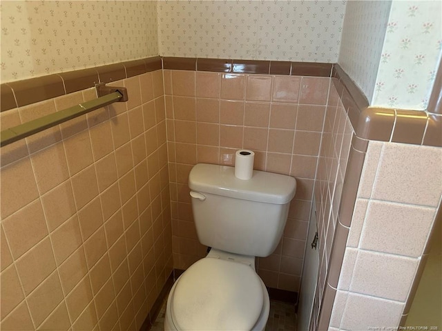 bathroom with wallpapered walls, tile walls, toilet, and a wainscoted wall