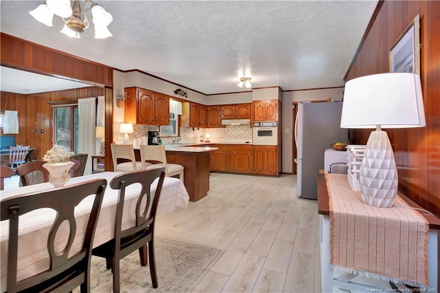 kitchen with under cabinet range hood, brown cabinets, freestanding refrigerator, and oven