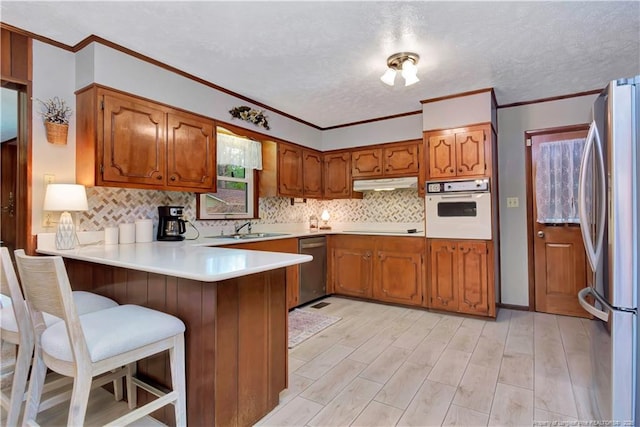 kitchen featuring under cabinet range hood, appliances with stainless steel finishes, brown cabinetry, and a peninsula