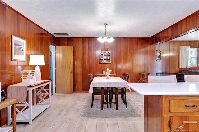 dining room featuring a notable chandelier, light wood-style floors, visible vents, and wood walls