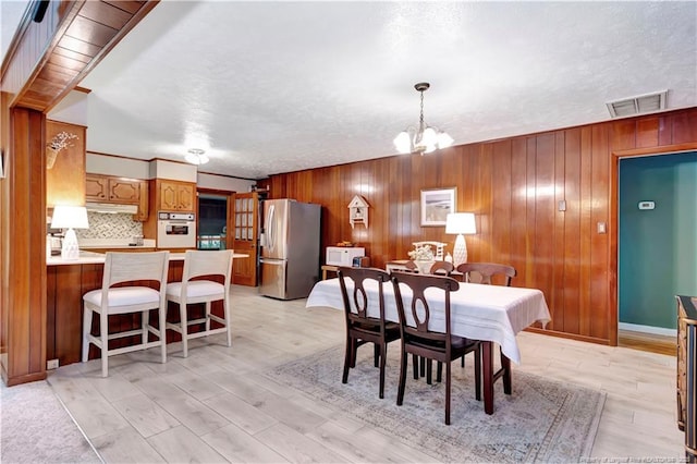 dining space featuring a chandelier, visible vents, wood walls, and light wood-type flooring