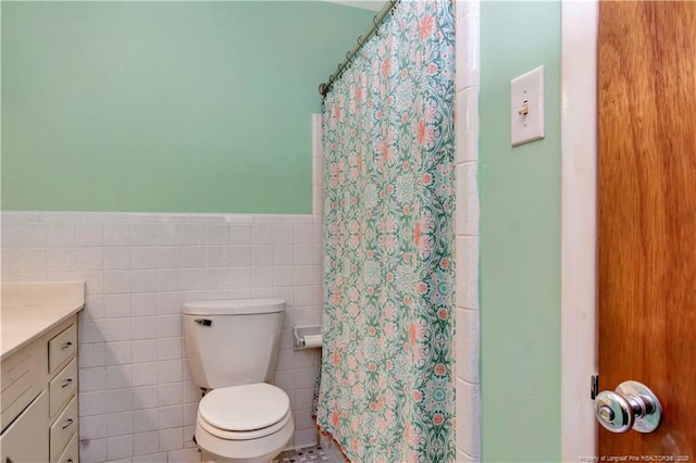 bathroom featuring a wainscoted wall, toilet, vanity, a shower with curtain, and tile walls