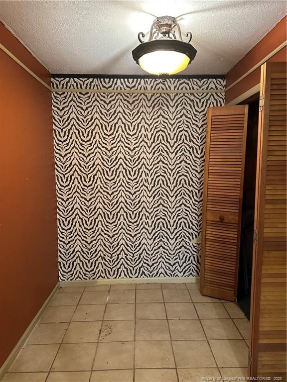 empty room featuring light tile patterned floors, baseboards, and a textured ceiling