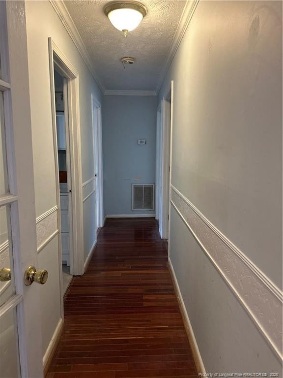 hallway with visible vents, a textured ceiling, crown molding, and wood finished floors