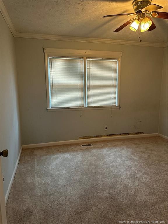 carpeted spare room featuring baseboards, visible vents, ceiling fan, a textured ceiling, and crown molding