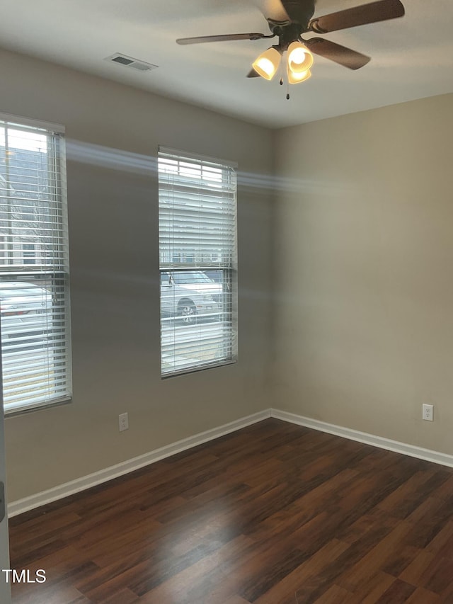 spare room featuring a wealth of natural light, baseboards, ceiling fan, and dark wood-style flooring