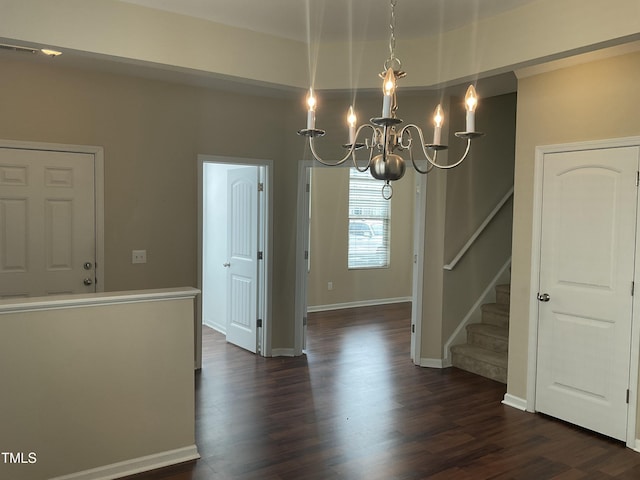 unfurnished dining area with dark wood finished floors, an inviting chandelier, stairway, and baseboards