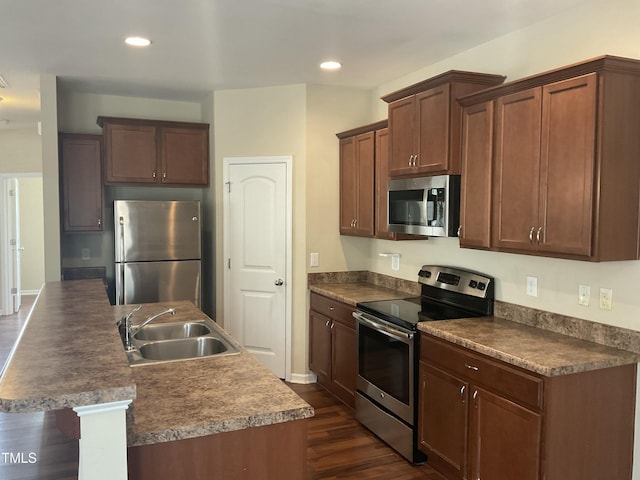 kitchen with a center island with sink, dark wood finished floors, recessed lighting, a sink, and appliances with stainless steel finishes