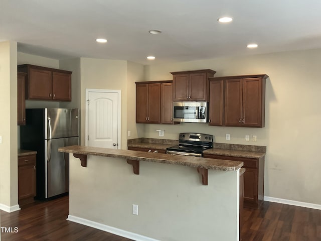 kitchen with dark wood finished floors, appliances with stainless steel finishes, and a breakfast bar area