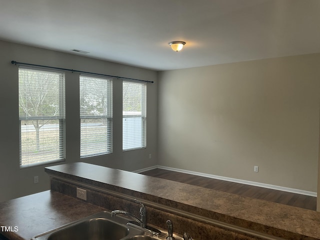 kitchen with dark countertops, visible vents, baseboards, dark wood-style floors, and a sink