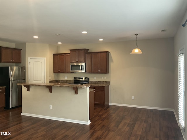 kitchen with baseboards, appliances with stainless steel finishes, a breakfast bar, and dark wood-style flooring