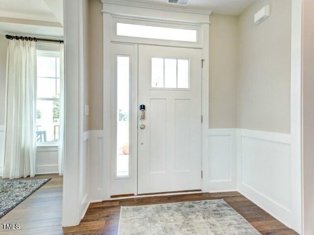 entrance foyer featuring dark wood-style floors, a decorative wall, wainscoting, and visible vents