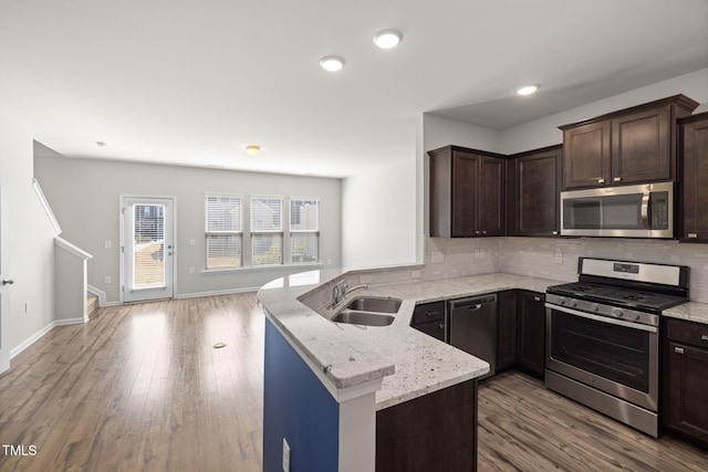 kitchen featuring a sink, stainless steel appliances, dark brown cabinetry, a peninsula, and decorative backsplash