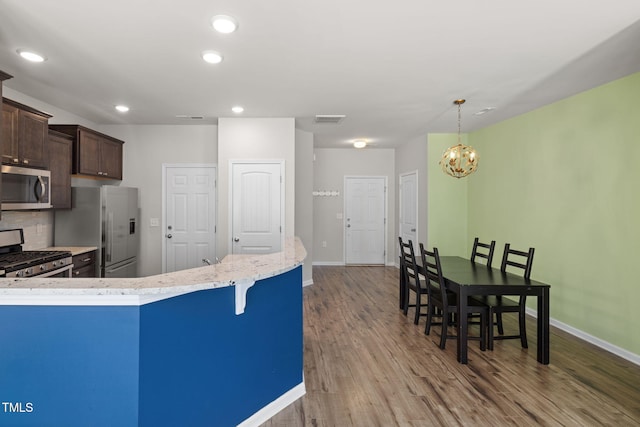 kitchen with visible vents, backsplash, wood finished floors, appliances with stainless steel finishes, and dark brown cabinets