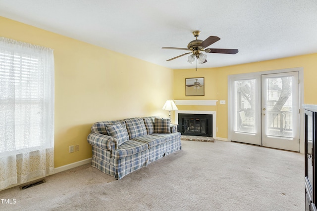 carpeted living room featuring visible vents, baseboards, a ceiling fan, and a fireplace