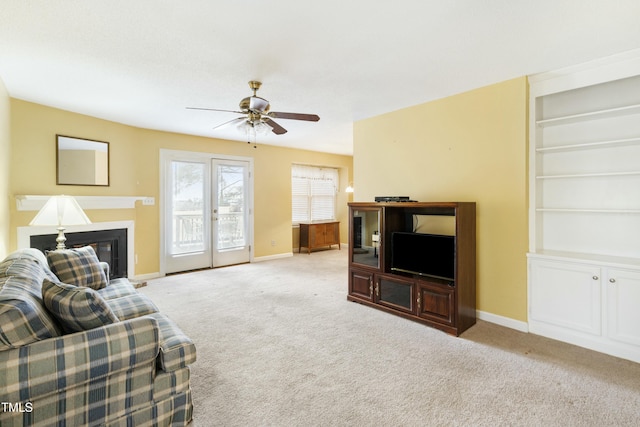 carpeted living room featuring a glass covered fireplace, a ceiling fan, and baseboards