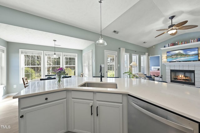 kitchen featuring lofted ceiling, a tile fireplace, hanging light fixtures, a sink, and dishwasher