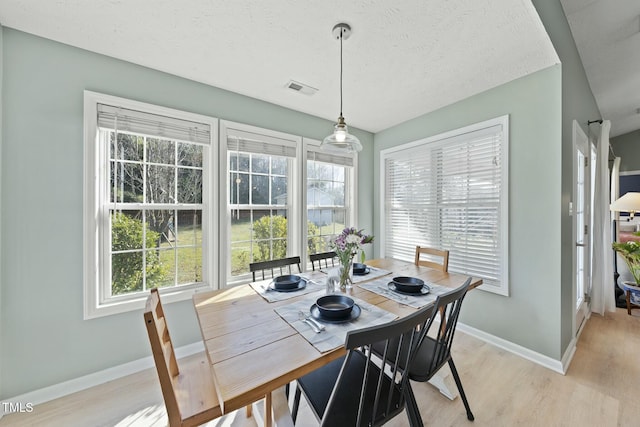 dining space with light wood-style flooring, baseboards, visible vents, and a textured ceiling