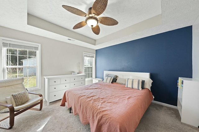 bedroom with light carpet, visible vents, a textured ceiling, and a tray ceiling