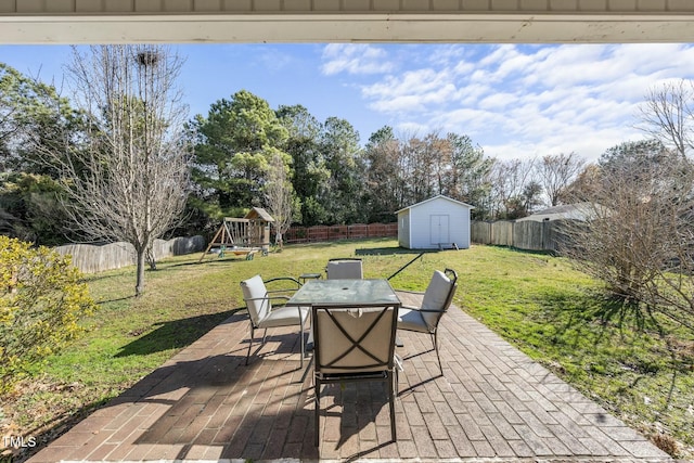 view of patio featuring outdoor dining space, a fenced backyard, an outdoor structure, a storage shed, and a playground