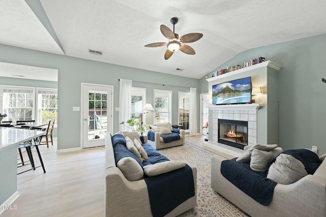 living area featuring visible vents, ceiling fan, light wood-type flooring, lofted ceiling, and a tile fireplace