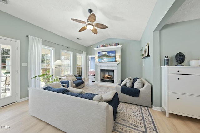 living room featuring a tiled fireplace, light wood-type flooring, ceiling fan, and vaulted ceiling