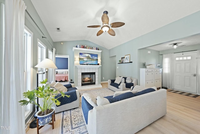 living room with wood finished floors, a ceiling fan, visible vents, lofted ceiling, and a tiled fireplace