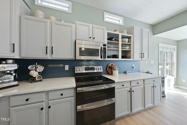 kitchen featuring open shelves, light wood-style flooring, light countertops, appliances with stainless steel finishes, and a textured ceiling