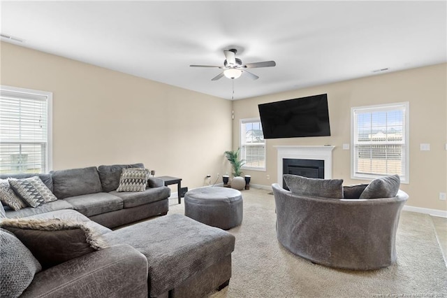 living room featuring visible vents, baseboards, ceiling fan, light carpet, and a glass covered fireplace