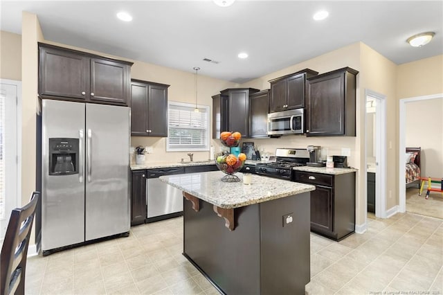 kitchen featuring light stone counters, stainless steel appliances, hanging light fixtures, dark brown cabinets, and a center island