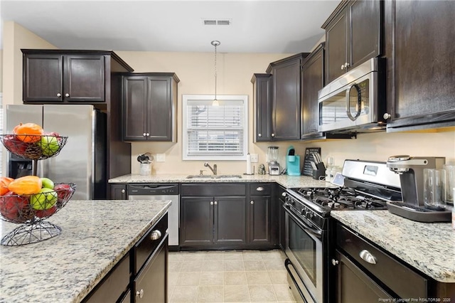 kitchen with dark brown cabinets, appliances with stainless steel finishes, light stone countertops, and a sink