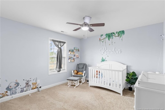 carpeted bedroom featuring visible vents, a crib, baseboards, and a ceiling fan