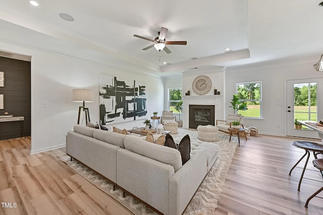 living area with baseboards, light wood-type flooring, a raised ceiling, and a ceiling fan