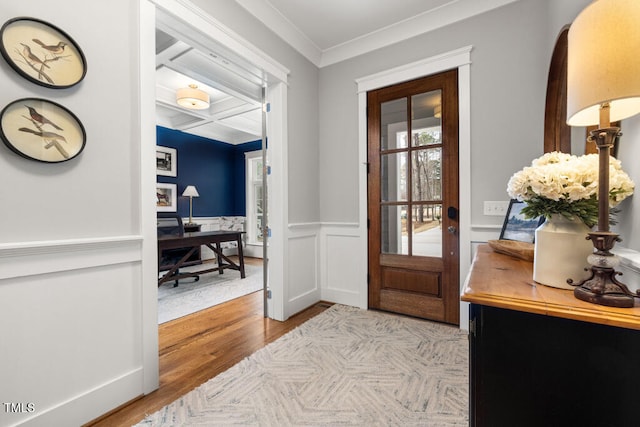 doorway with beamed ceiling, ornamental molding, wainscoting, wood finished floors, and coffered ceiling