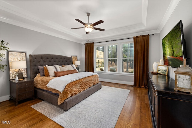 bedroom featuring ceiling fan, baseboards, ornamental molding, wood finished floors, and a raised ceiling