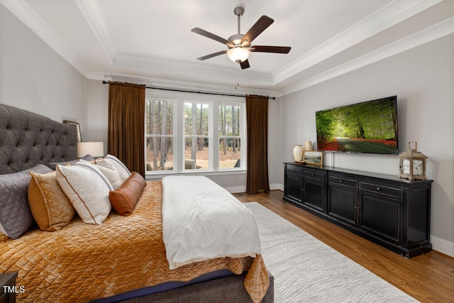 bedroom with a raised ceiling, crown molding, wood finished floors, and baseboards