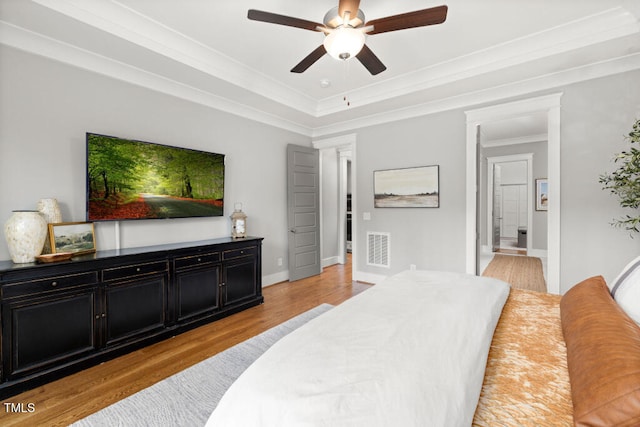 bedroom featuring visible vents, light wood-style flooring, a tray ceiling, crown molding, and baseboards