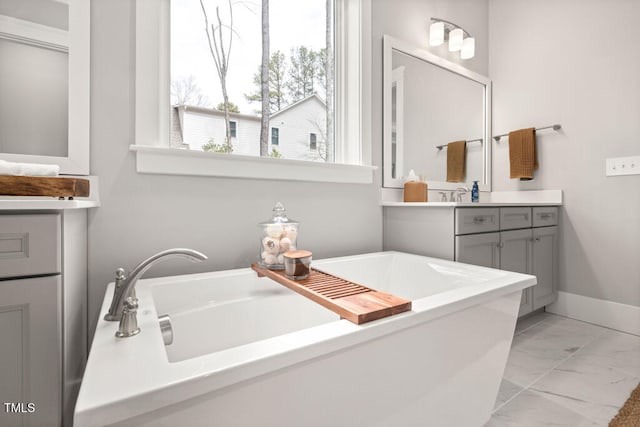 full bath featuring marble finish floor, a washtub, vanity, and baseboards