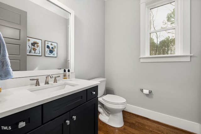 half bath with baseboards, toilet, wood finished floors, and vanity