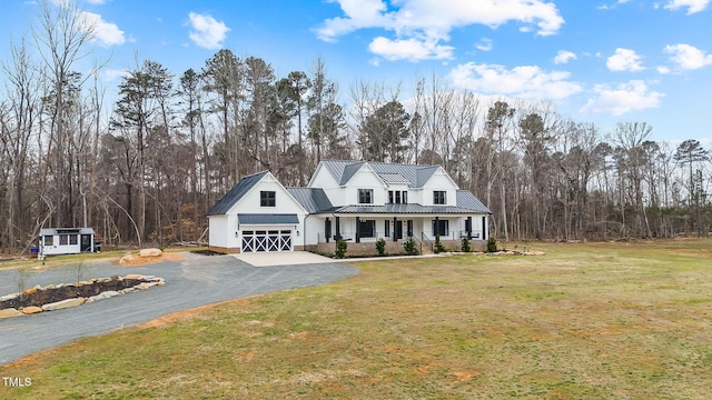 view of front of home featuring a front yard, covered porch, metal roof, driveway, and a standing seam roof