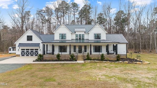 modern inspired farmhouse with driveway, a standing seam roof, covered porch, a front yard, and metal roof