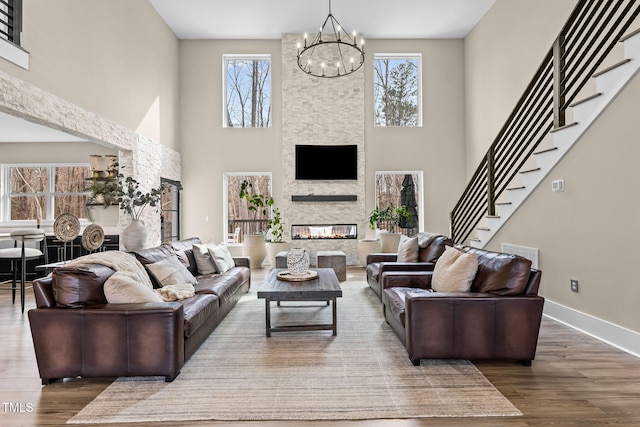 living room with wood finished floors, an inviting chandelier, a fireplace, baseboards, and stairs