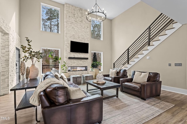 living area with wood finished floors, baseboards, an inviting chandelier, a fireplace, and stairs