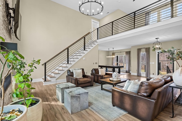 living area with stairway, a high ceiling, an inviting chandelier, and wood finished floors