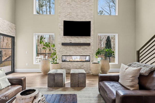 living area with wood finished floors, a fireplace, baseboards, and a towering ceiling