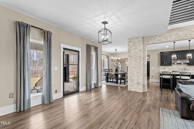 living area featuring baseboards, a notable chandelier, a healthy amount of sunlight, and wood finished floors