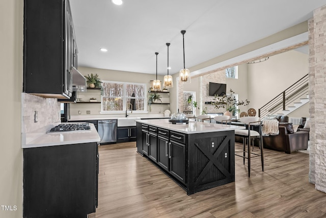 kitchen featuring open floor plan, dark cabinets, light countertops, stainless steel appliances, and open shelves