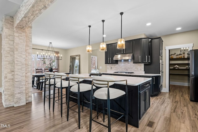 kitchen with under cabinet range hood, freestanding refrigerator, ornate columns, and dark cabinets