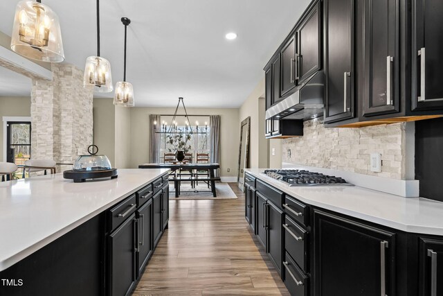 kitchen with backsplash, under cabinet range hood, stainless steel gas cooktop, light countertops, and dark cabinets