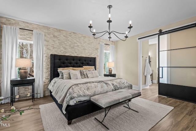 bedroom with a barn door, light wood-style flooring, a notable chandelier, and baseboards